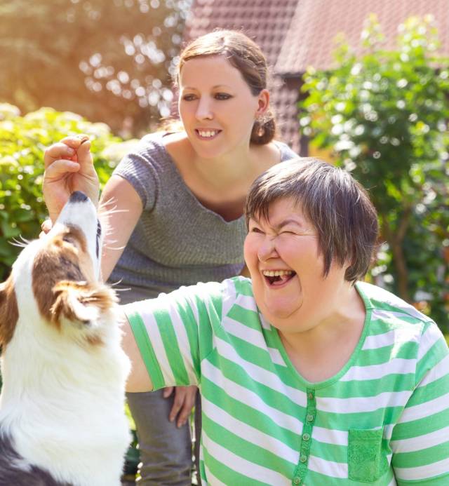 Alternativetherapie mit einem Hund, geistig behinderte Frau und Therapeutin im Garten